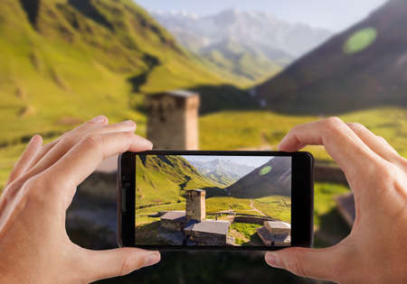 Travel concept. Hands making photo of Svaneti Old village in Georgia. Medieval tower built for defensive purposes.の写真素材