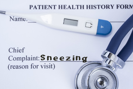 Chief complaint sneezing. Paper patient health history form, on which is written the complaint sneezing as the main reason for visit to the doctor, with a thermometer and stethoscopeの写真素材