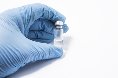 Transparent vial or bottle with the vaccine is in the doctor's hand, which is dressed in blue medical gloves. The concept of vaccination, research or production of vaccines against various diseasesの写真素材