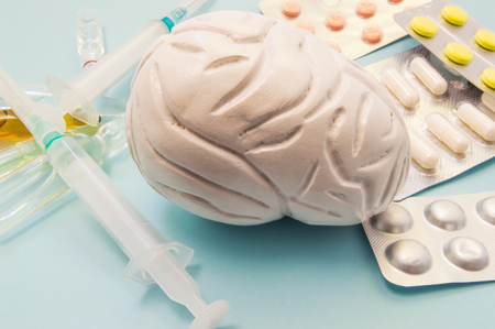 Brain treatment concept photo. Figure of brain surrounded by pills, medications, medicine vials with...