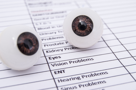 Figures of the two eyes (eyeball) lies on a white sheet of health history with the words vision problem. A visit to the eye doctor, ophthalmologist or optometrist. Ophthalmic image concept.の写真素材
