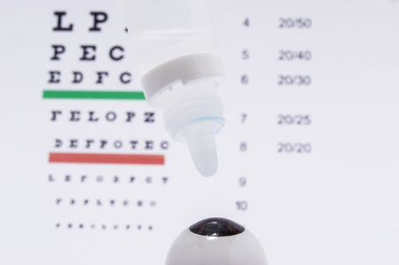 The figure of the eyeball with eye drops over it on the background of the table for visual acuity testing. Diagnosis and treatment of eye diseases or allergyの写真素材