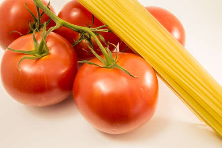 Tomatoes and pasta. A branch of the fresh tomatoes from the garden and not cooked raw pasta spaghettiの写真素材