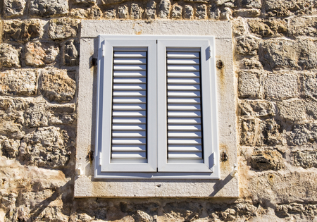 Closed PVC window with shutters on the wall of the old building of white coquina (shell limestone)...