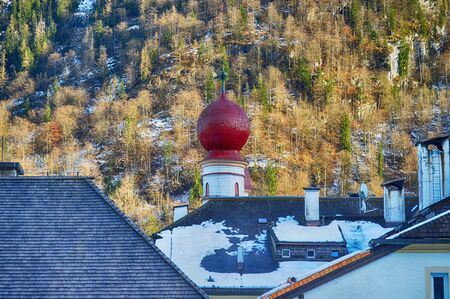 Red-purple dome of the Church on the background of wooded mountains in Alpsの写真素材