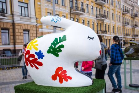Easter bunny figure in white with red, blue and green leaves with closed eyes on background of considering people. Beautiful easter decoration art .Kyiv (Kiev), Ukraine, april 2018のeditorial素材