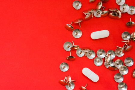 White pills surrounded by sharp thumbtacks at distance from them is on red background with empty area for headers top view. Concept images illustrating effect of painkillers and struggle with painの写真素材