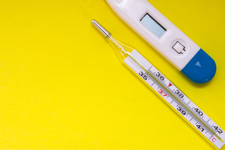 Two medical thermometer-mercury and electronic, are on uniform yellow background with  clean empty area for labels or headers top view. Concept photo to use inflammatory diseases accompanied by feverの写真素材