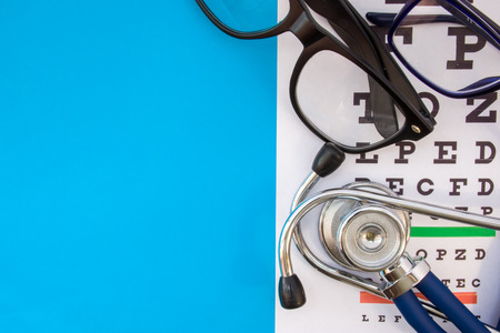 Snellen chart with pair of eyeglasses and stethoscope on blue background occupy half of photo, in second half empty space for titles. Concept photo of check visual acuity, optometry and ophthalmologyの写真素材