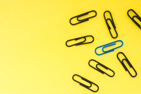 One blue clip and many black clips on yellow uniform background view from above with clear area of half of photo for labels or headers. Concept photo to highlight, not to be like at allの写真素材