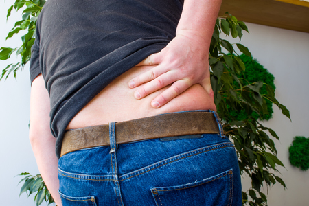 Concept of backaches, back pain or manifestations or symptoms of radiculopathy. Man grabbed with Palm over lumbar region on back, indicating localization of pain in spine pathologyの写真素材