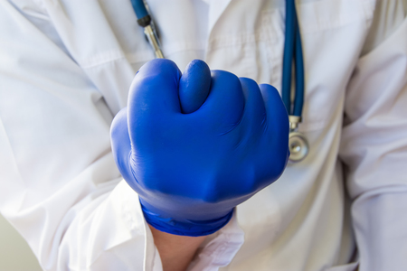 Doctor showing fig sign closeup. Doctor, scientist or researcher in a white lab coat and blue gloves demonstrated fig sign, folding fingers of palms to corresponding figure in the foregroundの写真素材