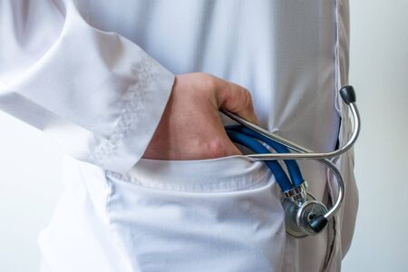 Doctor in white coat places right hand with stethoscope in palm into pocket side view. Concept photo...