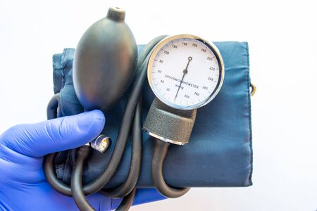 Medical professional, nurse or doctor holds in hand, wearing blue medical glove, blood pressure meter for measures blood pressure on white background. Concept for diagnosis of arterial hypertensionの写真素材