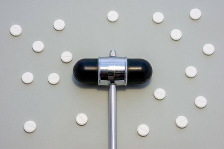 Head of reflex hammer is on gray background surrounded by pills or tablets with ornament of polka...