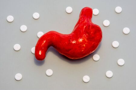 Anatomical figure of stomach, identical shape of live organ, is on gray background surrounded by white pills, components polka dots ornament. Photos for use in gastroenterology, concept for treatmentの写真素材