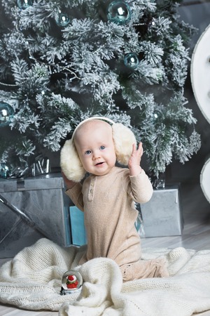 Happy little boy with fur headphones. under the Christmas tree