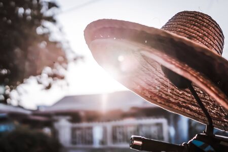 A farmer`s hat belongs to my grandma hanging on the rear mirror of motorcycle while sunlight behind hat at a  agriculture hometown Kampung Chui Chak, Perak, Malaysiaの写真素材