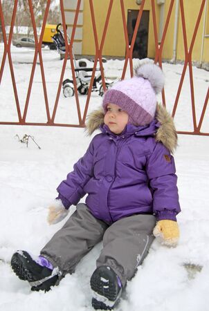 Child in lilac winter clothes sitting in the snowの写真素材