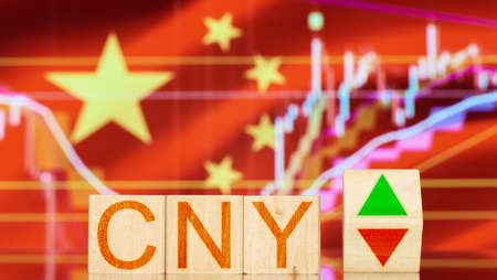 cny. wooden blocks with cny lettering and symbols of the rise and fall of foreign exchange markets against the background of the flag of chinaの写真素材