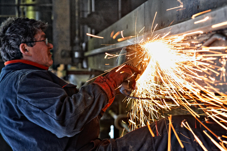 Handyman with electric grinder, grinding steel structure, focus on tools, low Lightの写真素材