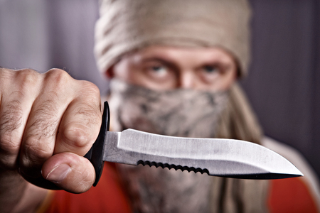 masked man holding a knife on a black background, focus forward