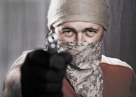 masked man holding a gun on a black background, focus on eyesの写真素材