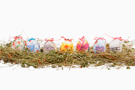 Easter colorful eggs with dry grass in the nest, isolated on whiteの写真素材