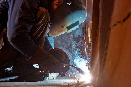 Welder working at the factory  in a welding mask and welders leathers