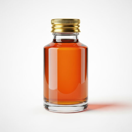 A clear glass miniature bottle containing a rich amber-colored liquid, topped with a shiny gold screw-on cap. This close-up shot highlights the beverage and its packaging.の素材