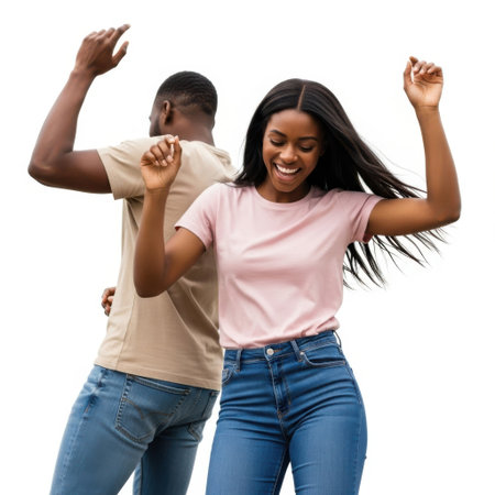 The image depicts a joyful couple dancing together. The man and woman are both smiling and appear to be enjoying their dance. They are dressed casually, with the man wearing a beige t-shirt and blue jeans, and the woman wearing a pink t-shirt and blue jeans. Their body language suggests they are having a great time, with their arms raised in the air as they dance.の素材