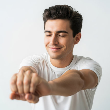 The image features a young man wearing a white t-shirt, stretching his arm forward. He has short, dark hair and appears to be in a relaxed and comfortable environment. The background is plain and white, which puts the focus entirely on the subject. The man has a slight smile on his face, suggesting a sense of contentment or enjoyment.の素材