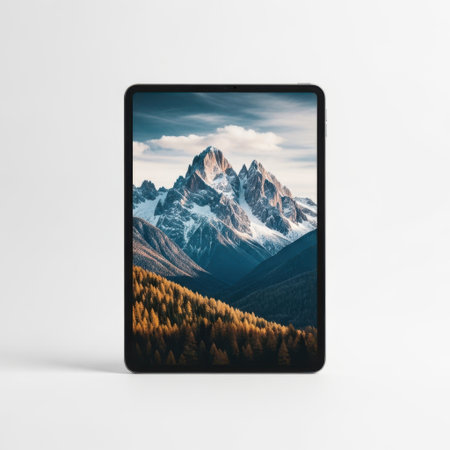 A tablet device displays a stunning image of a mountain landscape. The screen shows a majestic mountain range with snow-capped peaks, surrounded by a forest of autumn-colored trees. The sky above is partly cloudy, adding to the serene and picturesque scene.の素材