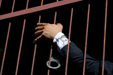 man in a black suit with handcuffs on his hands on a dark blue background in studio isolatedの写真素材