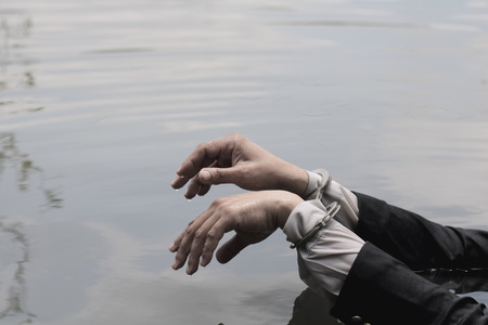Hand of a businessman handcuffed over water.の写真素材