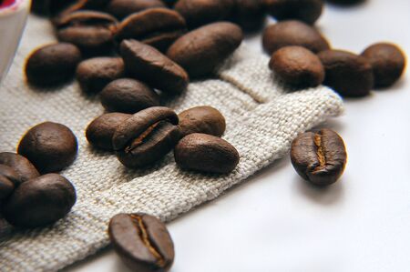 Large coffee brown beans of roasted coffee scattered on a linen napkin on the tableの写真素材