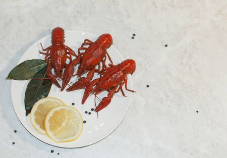 Appetizing plate with three red boiled crayfish, lemon slices and pepper on a marble white table