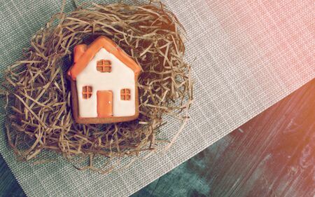 A small beautiful gingerbread house lies on a straw on a black tableの写真素材