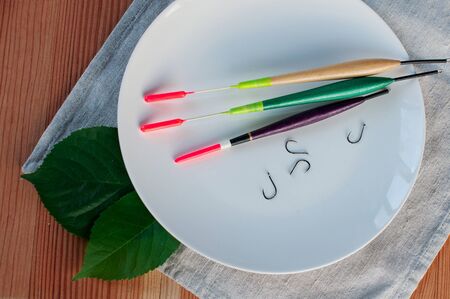 Fishing colored floats lie on a white plate on a wooden table