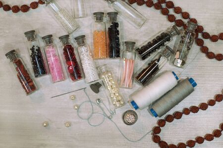 Bright little glass jars with colored beads and tools for needlework lie on a gray wooden table