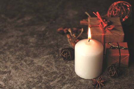 Red and white festive candles burn with a yellow flame on the table among gifts in craft paper,...
