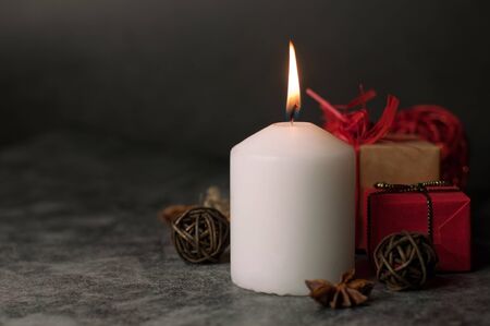 Red and white festive candles burn with a yellow flame on the table among gifts in craft paper, rattan balls, cinnamon sticks and anise starsの写真素材