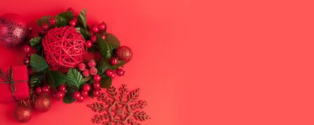 Christmas festive red background with a fir branch, under which are gifts in craft paper among Christmas decorations, toys and snowflakesの写真素材