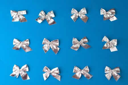 Christmas festive blue background, on which lies a group of Christmas tree decorations, silver bows at the same distance from each otherの写真素材