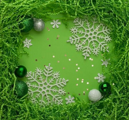 Christmas plain green background with green balls, with a frame of cut corrugated paper and white snowflakesの写真素材