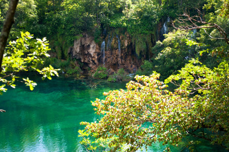 Lake with transparent emerald water. Waterfall among red rocks and foliage. Plitvice lakes national park, Croatiaの写真素材