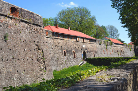 High stone walls of the Uzhhorod castle among green trees and hedge. Warm sunny spring days, cloudless blue skyの写真素材