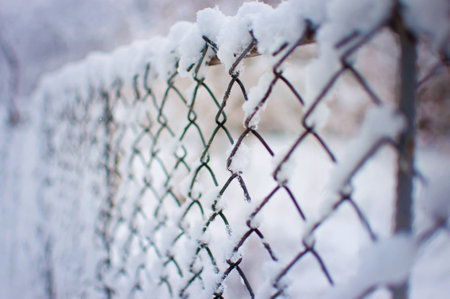 Closeup of a mesh fence covered in a thick layer of white fresh fluffy snow against a blurred purple background. Cold winter day in Januaryの写真素材