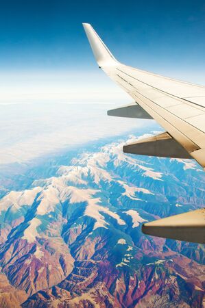 White airplane wing. Aerial view of majestic mountain range with yellow peaks, green and red forest, fields, blue sky and horizon. Sunny cloudless autumn day. Carpathian mountains, Romaniaの写真素材