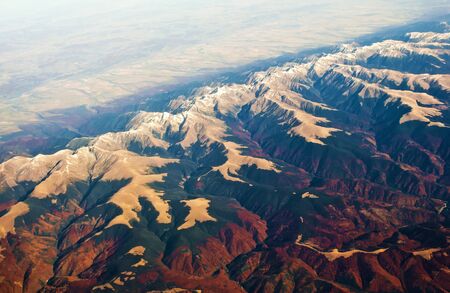 Aerial view of majestic Carpathian mountain range with snow-capped peaks and hills, green and red forest, fields. Sunny cloudless autumn day. Shot above Romaniaの写真素材
